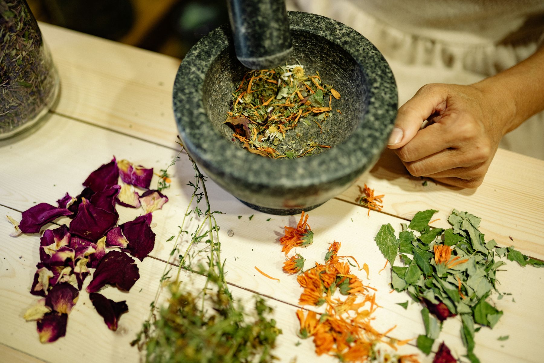 Herbs and dried flower petals being ground in a stone mortar and pestle